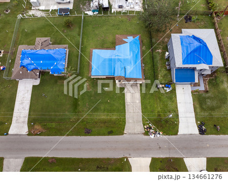 Top view of leaking house roof covered with protective tarp sheets against rain water leaks until replacement of asphalt shingles. Damage of building rooftop as aftermath of hurricane in Florida 134661276