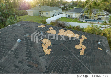 Ruined rooftop in need of repair. Wind damaged house roof with missing asphalt shingles after hurricane Ian in Florida 134661375