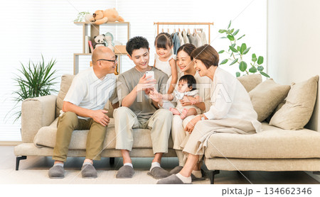 リビングルームでスマホを見ながらくつろぐ三世代家族,ファミリー（団らん） 134662346