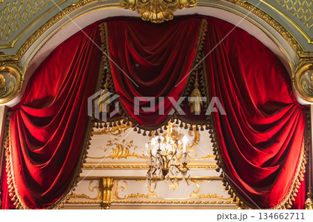 Opulent red velvet drapes framed by gilded architectural details 134662711