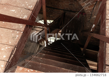 A dusty, weathered wooden staircase winds downward through a brick attic A dusty, weathered wooden staircase winds downward through a brick attic 134662718