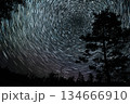 Star trails create mesmerizing patterns above a forest during a clear night sky 134666910