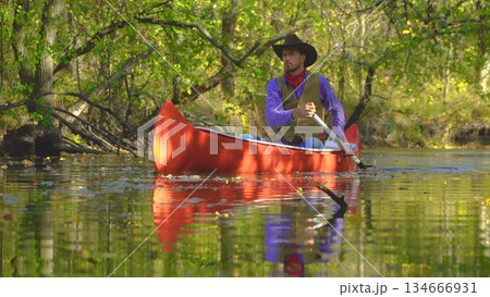 Cowboy in a canoe floats on the river in the forest Cowboy in a canoe floats on the river in the forest 134666931