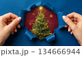 banner with women's hands tearing a bright blue sheet of paper, revealing a Christmas tree in the hole. Merry Christmas and Happy New Year greetings 134666944