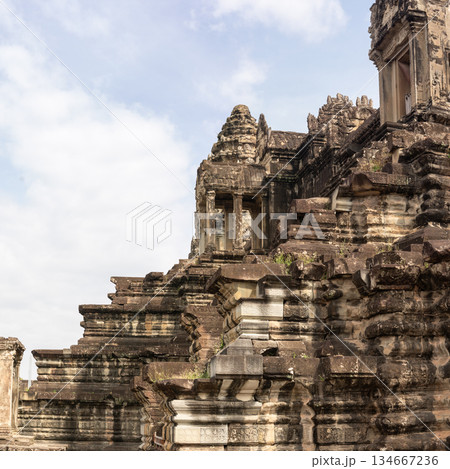 Side view of massive ancient stone temple structure with steep stairs and weathered walls under blue sky in Siem Reap 134667236