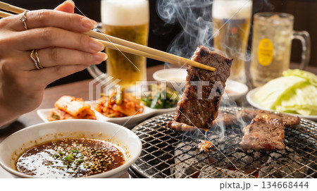 炭火で焼かれた熱々の焼肉を箸でつまむ手元とビール 134668444