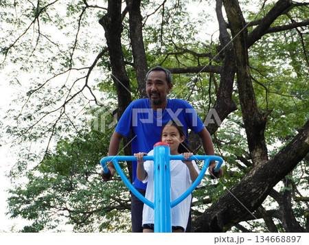 Father and daughter exercise on exercise equipment in an outdoor park. Father and daughter exercise on exercise equipment in an outdoor park. 134668897