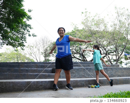 Mother and Daughter Stretching and Exercising with Dumbbells Outdoors 134668923
