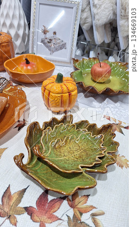 Artistic autumn-inspired ceramic dishes and pumpkin-shaped bowls displayed on a decorative table 134669103