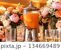 Elegant wedding beverage display with orange punch surrounded by floral arrangements 134669489