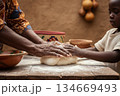 African mother and child baking together with dough on wooden table outdoors 134669493