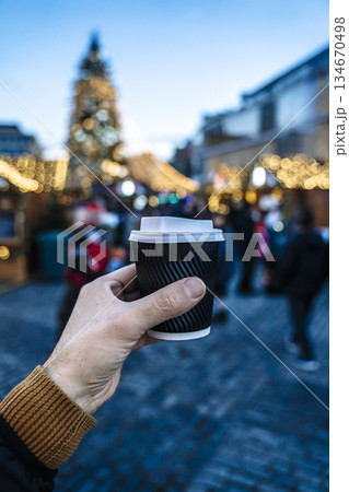 Hand Holding Hot mulled wine, Coffee, cocoa, tea, at Festive Christmas Market with Blurred Lights 134670498
