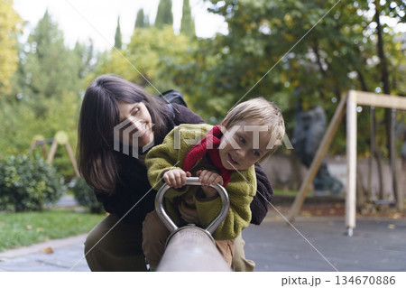 Happy Mother and Young Son Playing on Seesaw at Outdoor Playground Happy Mother and Young Son Playing on Seesaw at Outdoor Playground 134670886