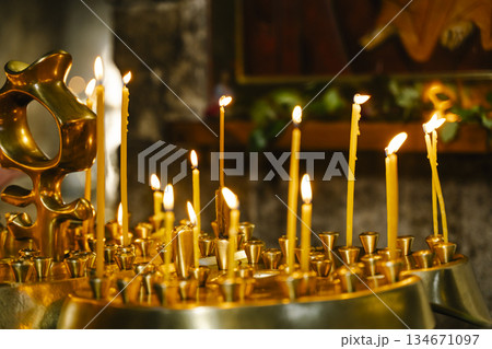Candles in a Christian Orthodox church background. Flame of candles in the dark sacred interior of the temple 134671097