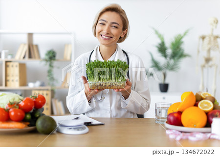 A smiling nutritionist holds a container of microgreens, surrounded by fresh fruits and vegetables, promoting healthy eating. A smiling nutritionist holds a container of microgreens, surrounded by fresh fruits and vegetables, promoting healthy eating. 134672022