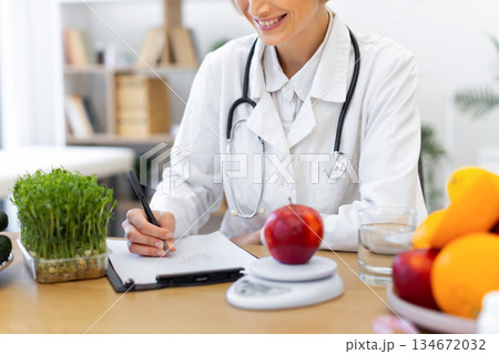 A dietitian smiles while writing a diet plan, surrounded by healthy food options. A dietitian smiles while writing a diet plan, surrounded by healthy food options. 134672032