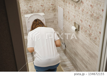 Young woman feeling unwell and experiencing nausea, leaning over toilet bowl Young woman feeling unwell and experiencing nausea, leaning over toilet bowl 134672155