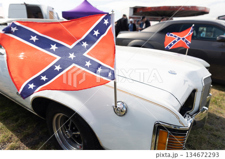 Confederate flag waving on white retro car at outdoor auto exhibition symbolic decoration vintage automobile details daylight. Historical reference and controversial emblem within classic car show Confederate flag waving on white retro car at outdoor auto exhibition symbolic decoration vintage automobile details daylight. Historical reference and controversial emblem within classic car show 134672293