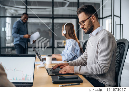 Focused, sitting by laptop. Professional workers are in the modern office together Focused, sitting by laptop. Professional workers are in the modern office together 134673057