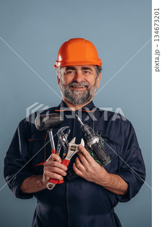Handyman is with tools. Senior man is standing in the studio against background 134673201