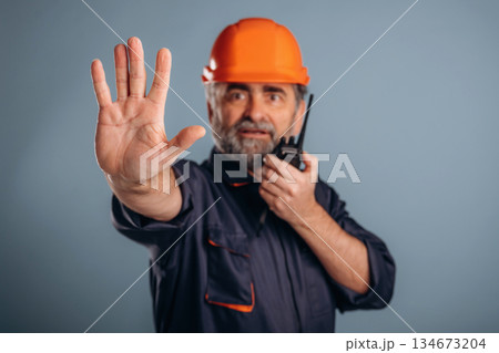 Worker is talking by walkie talkie. Senior man is standing in the studio against background Worker is talking by walkie talkie. Senior man is standing in the studio against background 134673204