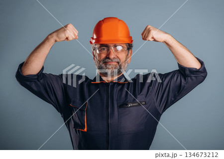 Strong, showing muscles, handyman. Senior man is standing in the studio against background 134673212