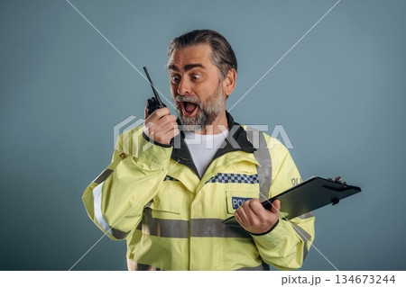 Construction worker is screaming into walkie talkie. Senior man is standing in the studio against background Construction worker is screaming into walkie talkie. Senior man is standing in the studio against background 134673244