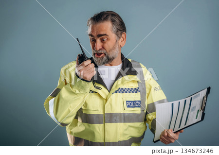Construction worker is screaming into walkie talkie. Senior man is standing in the studio against background Construction worker is screaming into walkie talkie. Senior man is standing in the studio against background 134673246