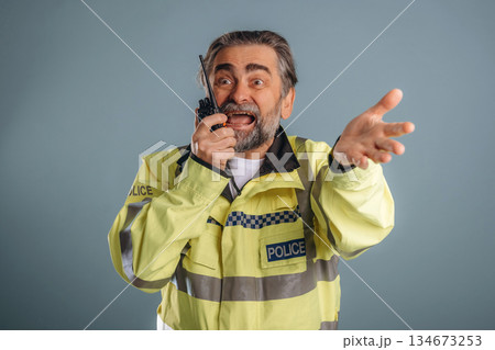 Talking into walkie talkie, police officer. Senior man is standing in the studio against background 134673253