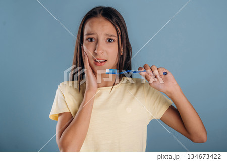 Pain in the tooth, holding toothbrush. Young girl is against background Pain in the tooth, holding toothbrush. Young girl is against background 134673422