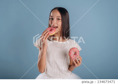 Two donuts in hands. Young girl in white dress is against background 134673471