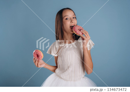 Two donuts in hands. Young girl in white dress is against background Two donuts in hands. Young girl in white dress is against background 134673472