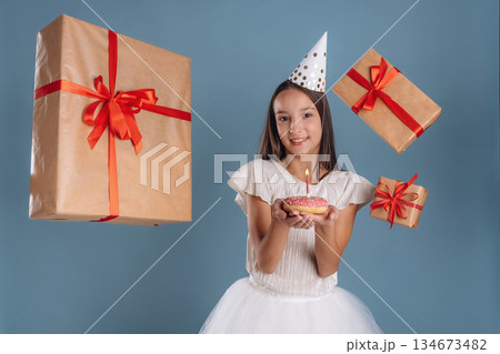 Bunch of gift boxes, happy birthday, donut with a candle. Young girl in white dress is against background Bunch of gift boxes, happy birthday, donut with a candle. Young girl in white dress is against background 134673482