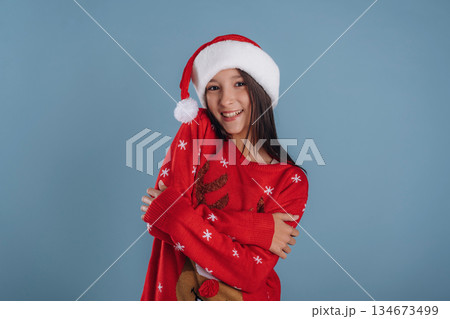 In Christmas clothes. Young girl is against background In Christmas clothes. Young girl is against background 134673499