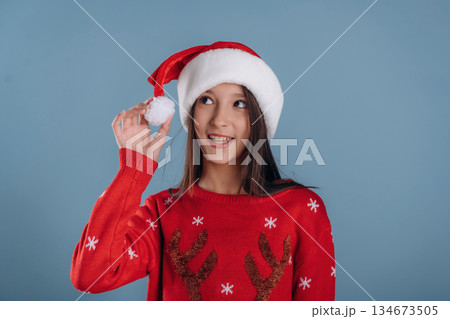 Santa hat. Young girl in Christmas clothes is against background 134673505