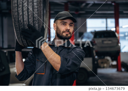Holding the tire. Mechanic working in a car service station Holding the tire. Mechanic working in a car service station 134673679