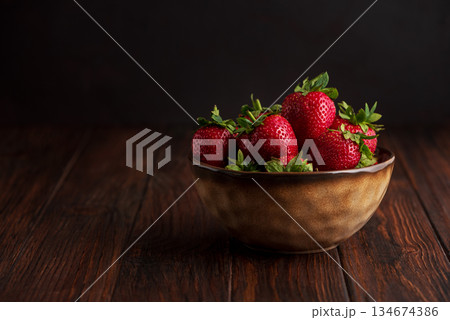 Fresh red strawberries in a rustic bowl on a dark wooden background. Front view 134674386