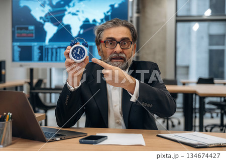 Time is running out, holding clock. Senior man is in the modern office 134674427