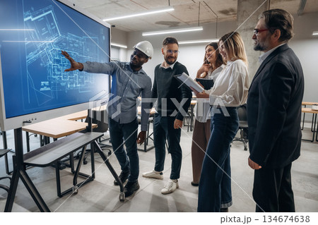 Building plan on screen. Group of office workers are indoors together Building plan on screen. Group of office workers are indoors together 134674638