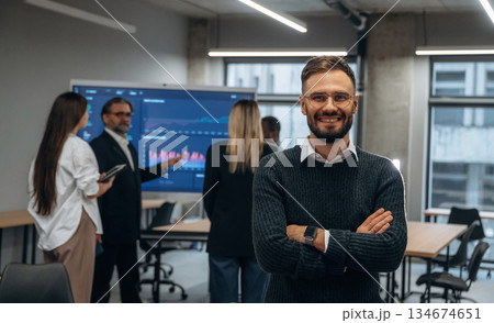 With arms crossed, standing against colleagues. Group of office workers are indoors together With arms crossed, standing against colleagues. Group of office workers are indoors together 134674651