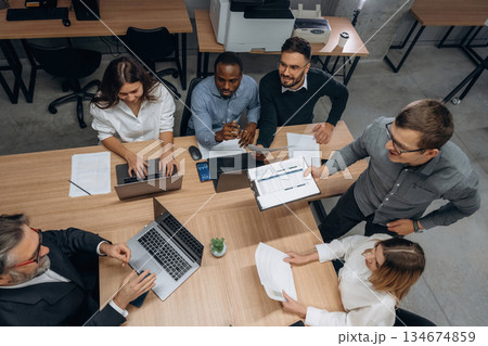 View from the top, by the table. Group of office workers are indoors together View from the top, by the table. Group of office workers are indoors together 134674859