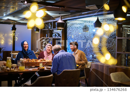 Families gather for iftar during Ramadan in a cozy restaurant setting, sharing food and laughter as the sun sets 134676268