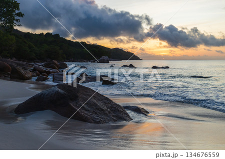 A peaceful coastal scene at sunset features smooth sand and rocks A peaceful coastal scene at sunset features smooth sand and rocks 134676559