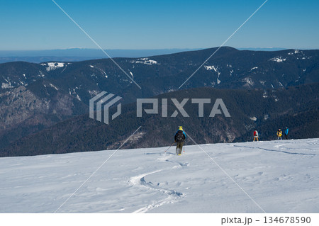 Skier standing on snowy mountain ridge overlooking vast winter landscape, wearing backpack and helmet, symbolizing adventure, freedom, backcountry skiing and alpine outdoor exploration 134678590