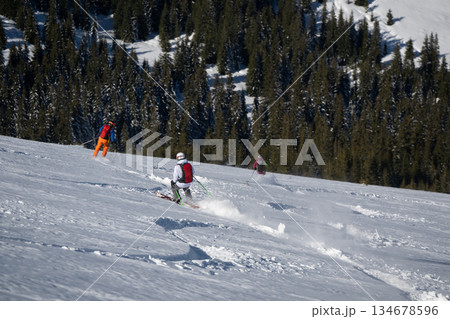 Skier skiing off piste through fresh powder on a sunny mountain slope, kicking up snow as she descends, creating a dynamic and energetic winter sports action scene under a clear blue sky Skier skiing off piste through fresh powder on a sunny mountain slope, kicking up snow as she descends, creating a dynamic and energetic winter sports action scene under a clear blue sky 134678596