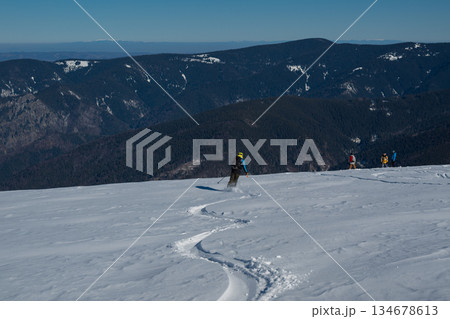 Skier standing on snowy mountain ridge overlooking vast winter landscape, wearing backpack and helmet, symbolizing adventure, freedom, backcountry skiing and alpine outdoor exploration 134678613
