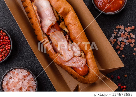 A hot dog with sausage, bacon, sauces, and a bun, unhealthy takeaway food. A hot dog with bacon 134678685