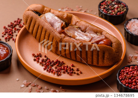 A hot dog with sausage, bacon, sauces, and a bun, unhealthy takeaway food. A hot dog with bacon 134678695