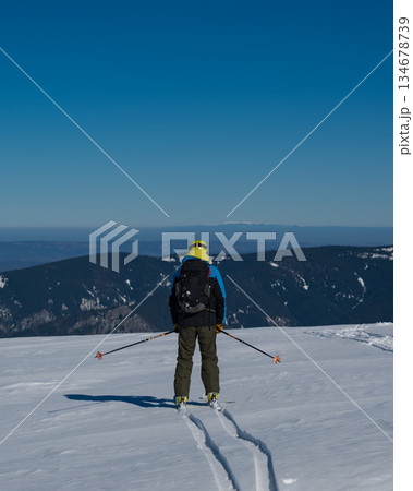 Skier standing on snowy mountain ridge overlooking vast winter landscape, wearing backpack and helmet, symbolizing adventure, freedom, backcountry skiing and alpine outdoor exploration Skier standing on snowy mountain ridge overlooking vast winter landscape, wearing backpack and helmet, symbolizing adventure, freedom, backcountry skiing and alpine outdoor exploration 134678739