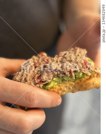 Hands holding tuna and avocado open sandwich with blurred background Hands holding tuna and avocado open sandwich with blurred background 134682049